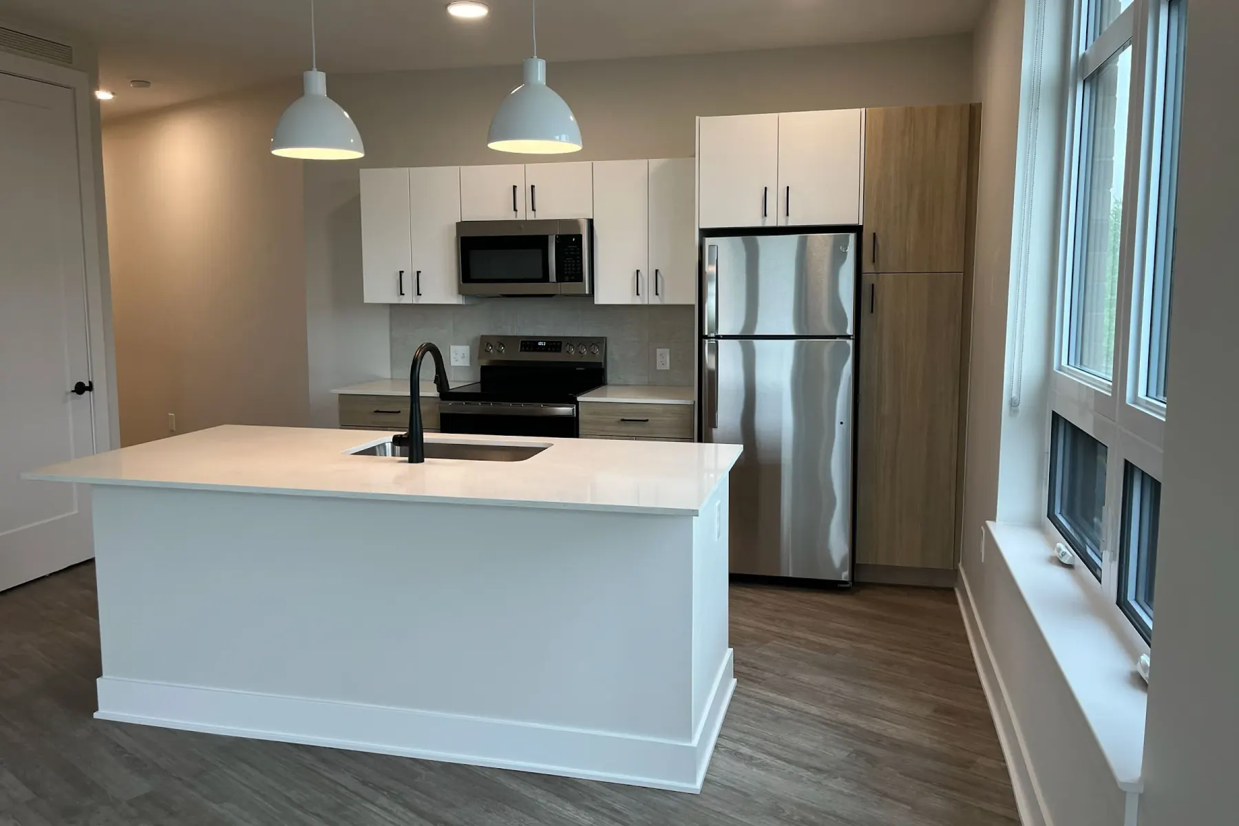 Packard Row apartment kitchen with white quartz island, stainless steel refrigerator and range, microwave, and wood-style flooring